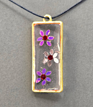 Resin pendant using bronze open bezels with flower inclusions.